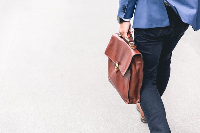 Walking man in blue suit carrying a leather brown briefcase