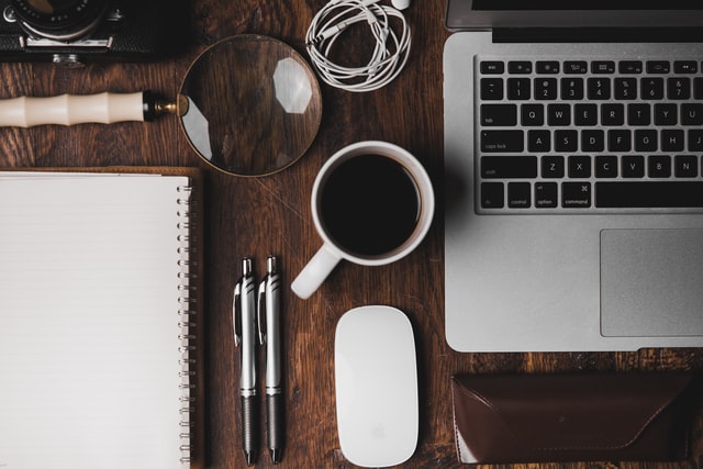 Wooden work desk with coffee, laptop, notebook, and pens